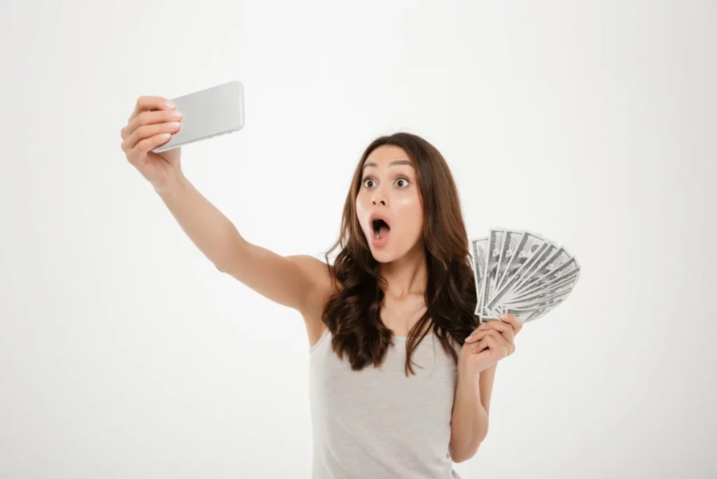 mulher segurando celular com uma mão e dinheiro na outra