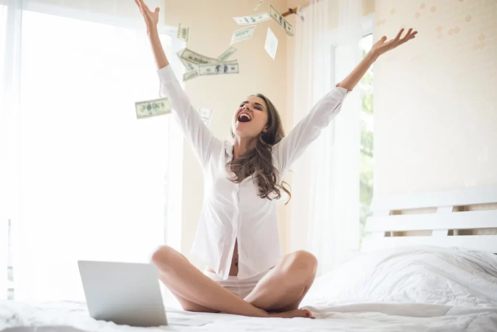 mulher na cama com notebook jogando dinheiro para cima