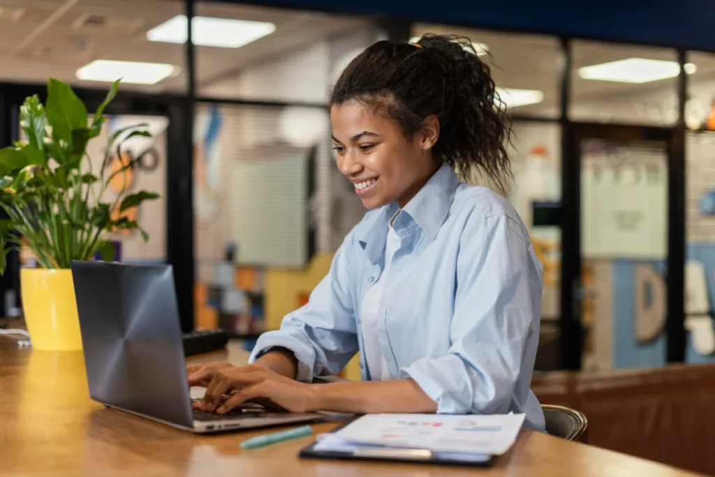 mulher negra em em sala de trabalho sorrindo ao computador - como vender com estratégias rápidas