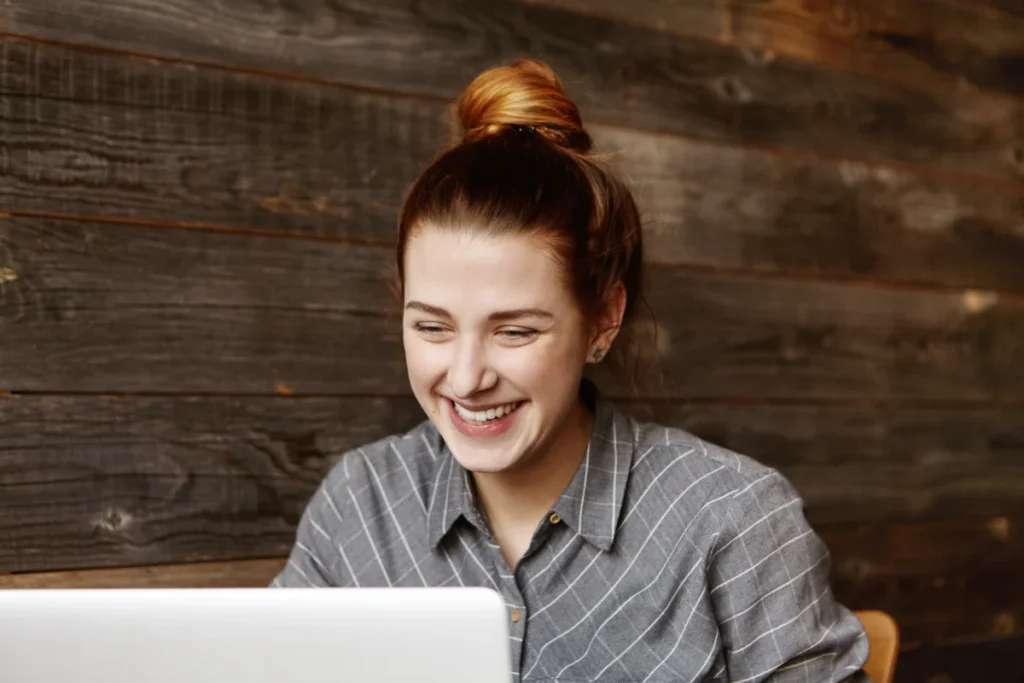 mulher ruiva com o cabelo preso sorrindo ao mexer no computador - como vender com estratégias rápidas
