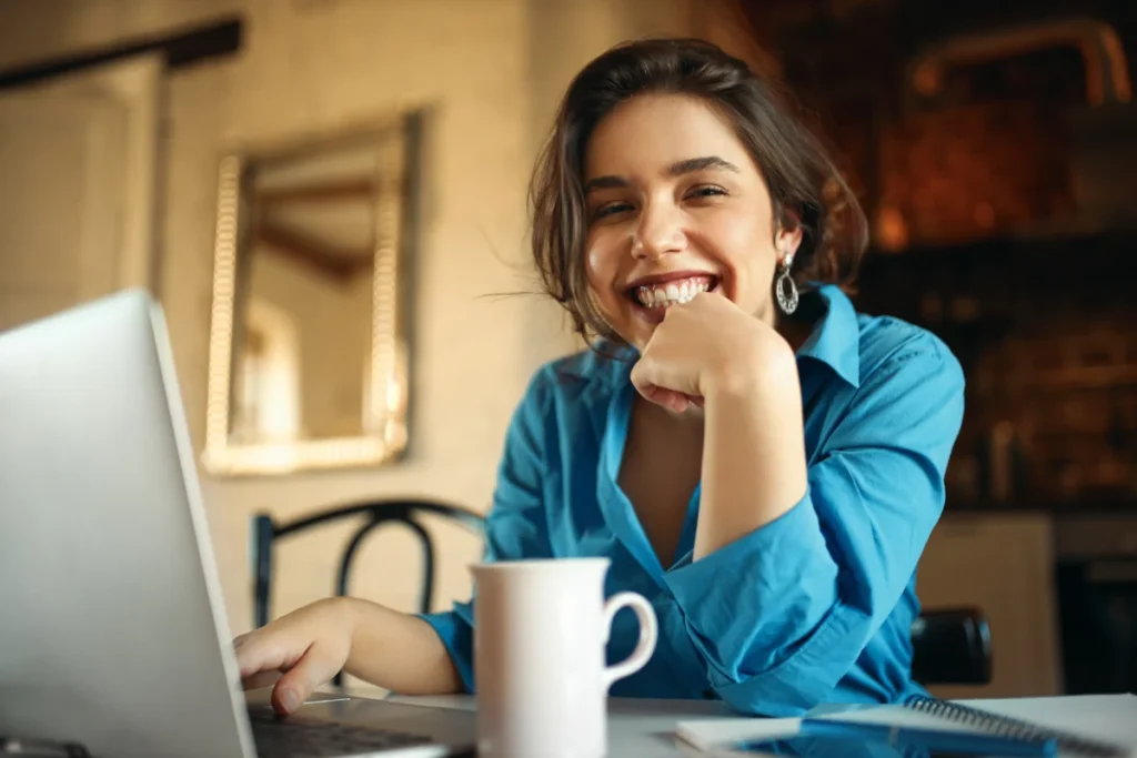 mulher jovem e sorridente com um café enquanto trabalha no computador como vender um produto