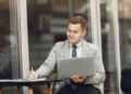 homem de negócios sentado ao ar livre mexendo no computador e anotando em papel - curso de marketplace