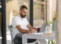 homem sentado em casa mexendo no computador e escrevendo em papel - amazon marketplace